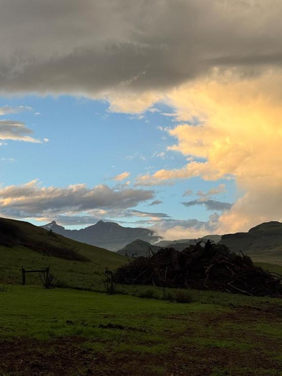 a field with a cloudy sky with mountains in the background at Scafell homestead, Cobham, Himeville in Ixopo