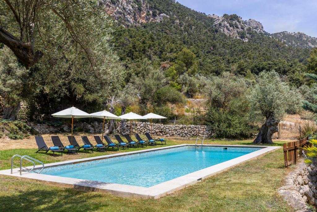 a pool with chairs and umbrellas next to a mountain at Honor - Rustic villa for 16 people in Bunyola