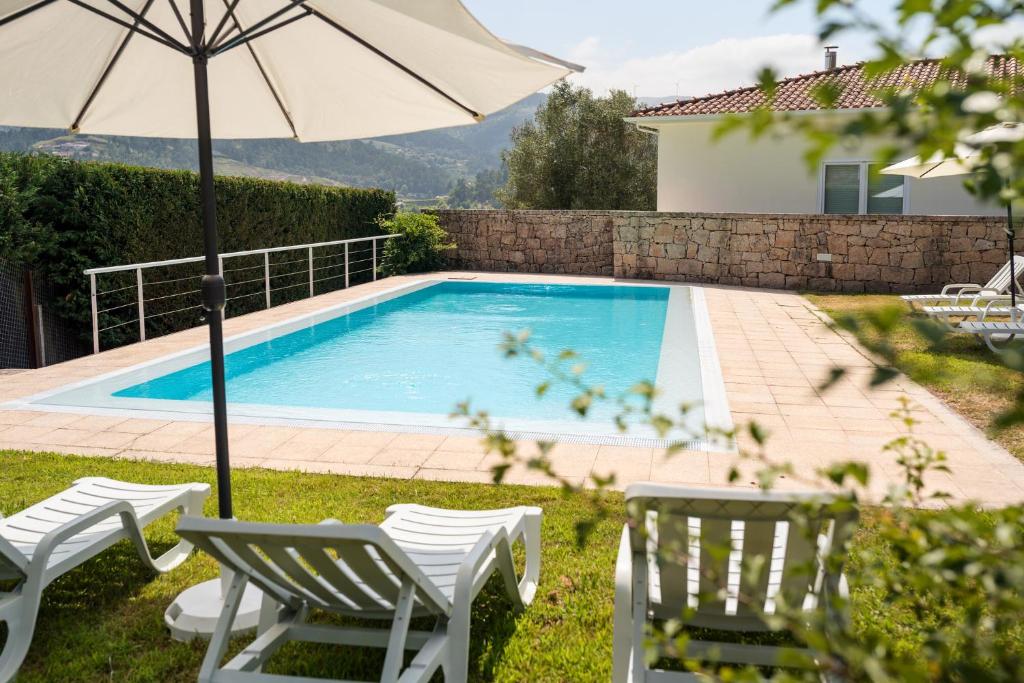 a swimming pool with two chairs and an umbrella at Casa Panorâmica Aurora in Celorico de Basto