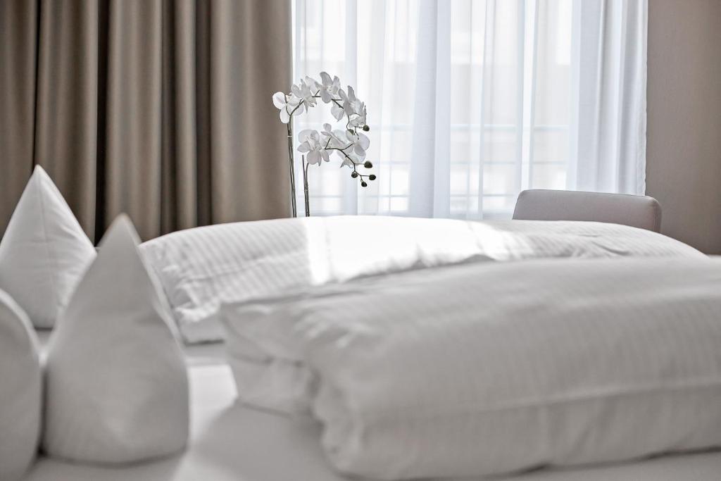 a white bed with white sheets and a vase of flowers at Hotel an der Stadtmauer in Schorndorf