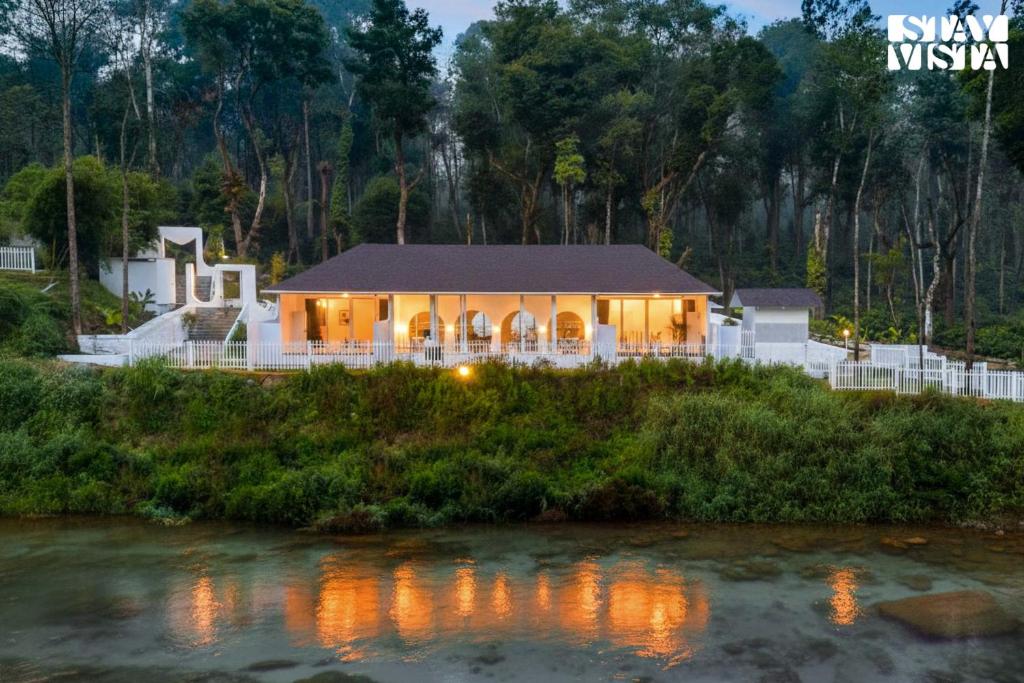 a house with lights on in front of a river at StayVista at Mudra Tattva - Pvt Pool,Lawn,Jacuzzi 2BR Luxury Rooms in Suntikoppa