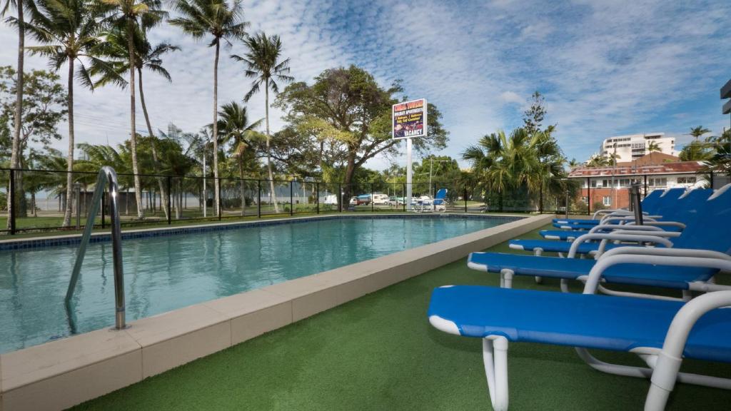 a swimming pool with blue chairs and palm trees at Coral Towers Holiday Suites in Cairns