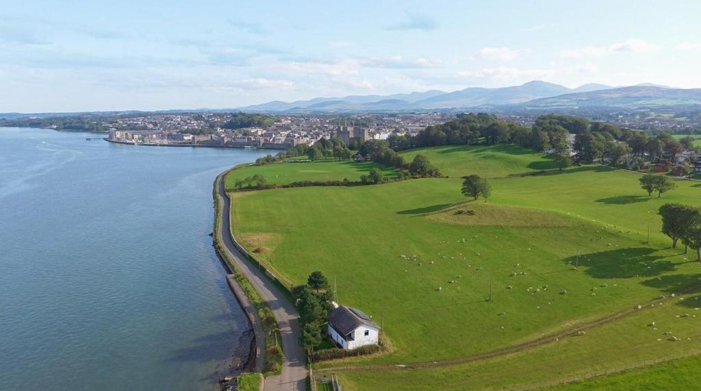 an aerial view of a green field next to a body of water at Bath Cottage in Caernarfon