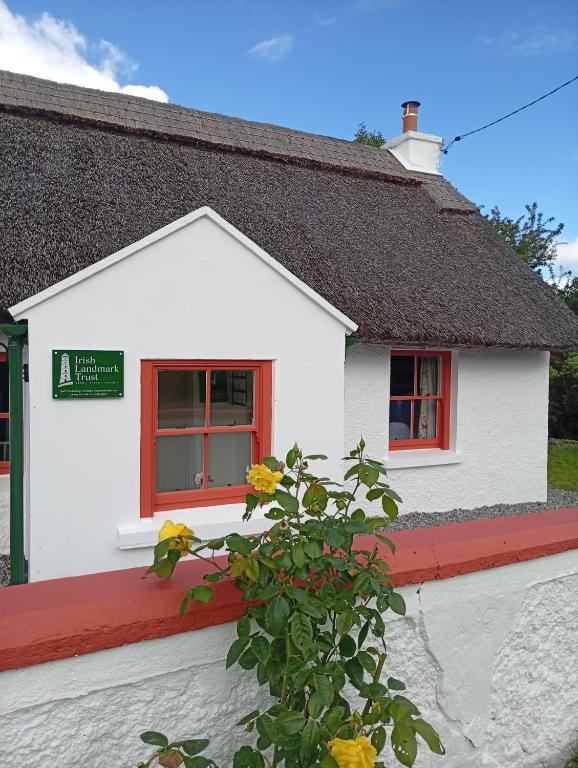a white house with red windows and a plant at Killee Cottage in Mitchelstown