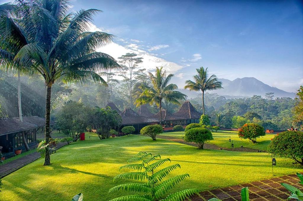 a lush green park with palm trees and buildings at MesaStila Resort and Spa in Borobudur