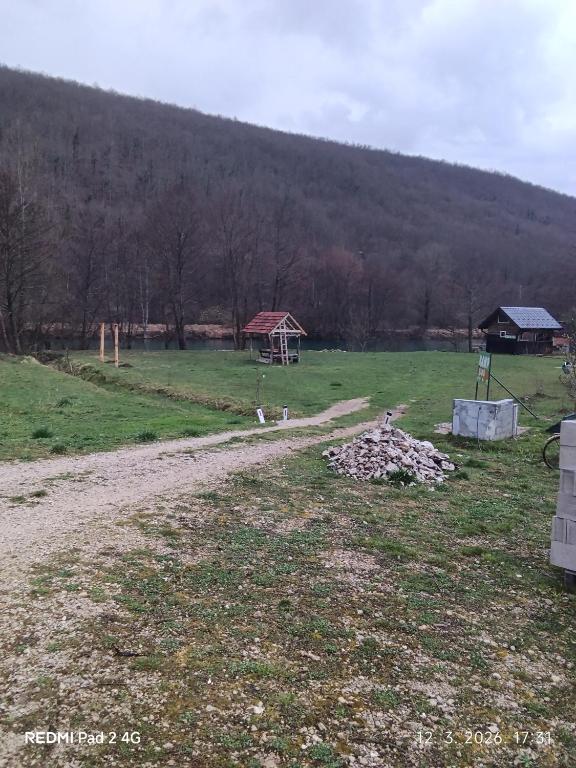 a dirt road in a field with a house in the background at Kamp Suad in Bihać