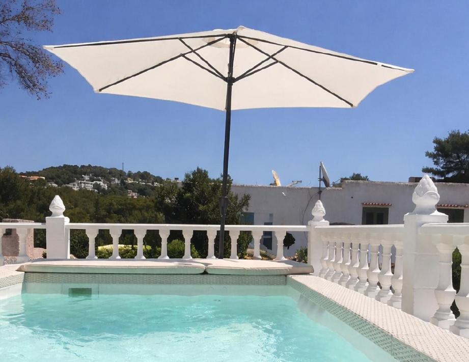 a white fence with an umbrella and a swimming pool at Can Fede in Cala Tarida