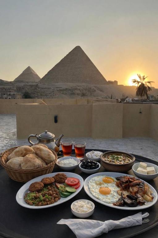 a table with plates of food with pyramids in the background at Monument Pyramids View in Cairo