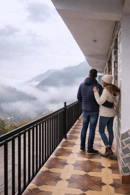 a man and woman standing on a balcony looking at the mountains at Milana Ashram in Jari