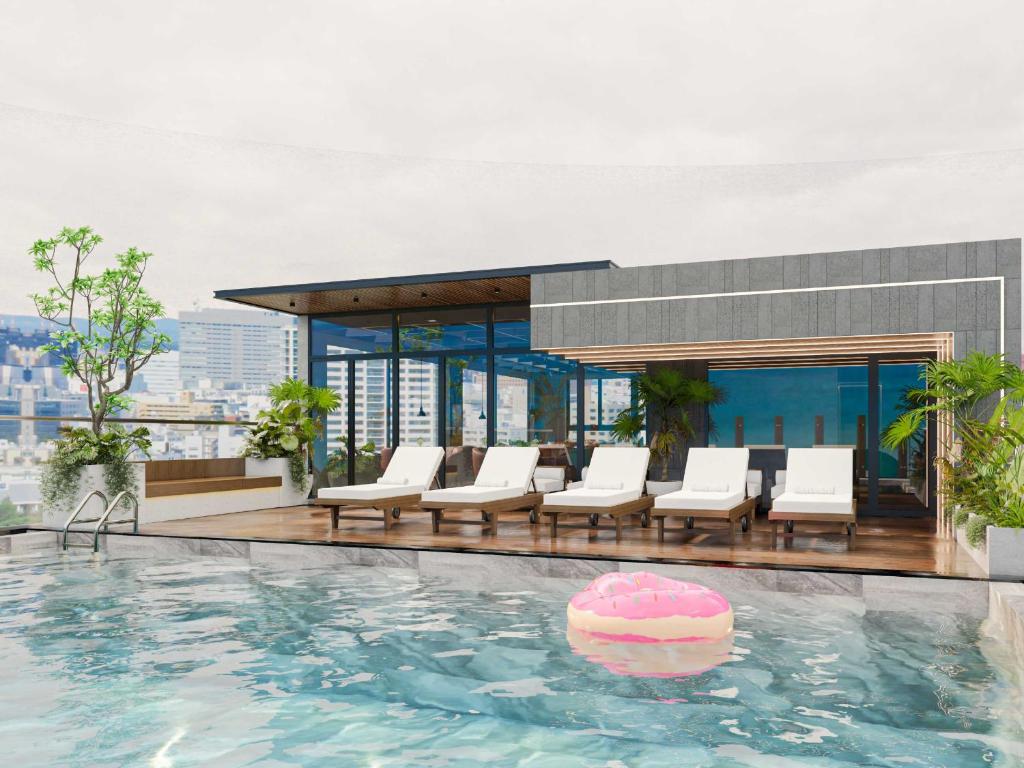 A rooftop pool terrace with loungers, greenery and a city backdrop.