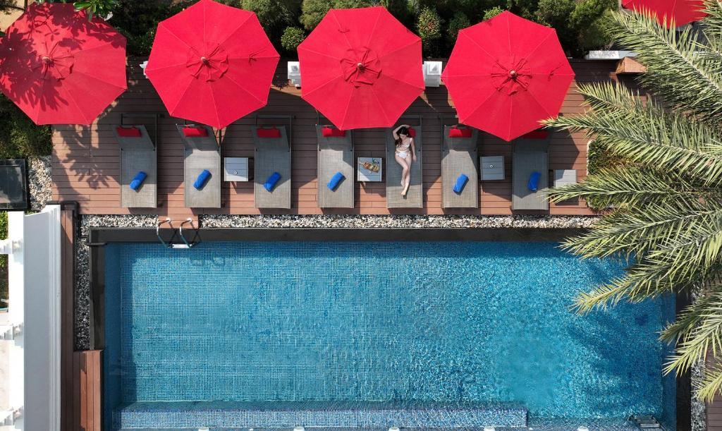 a woman standing next to a swimming pool with red umbrellas at March Hotel & Suite Riverside in Chiang Mai