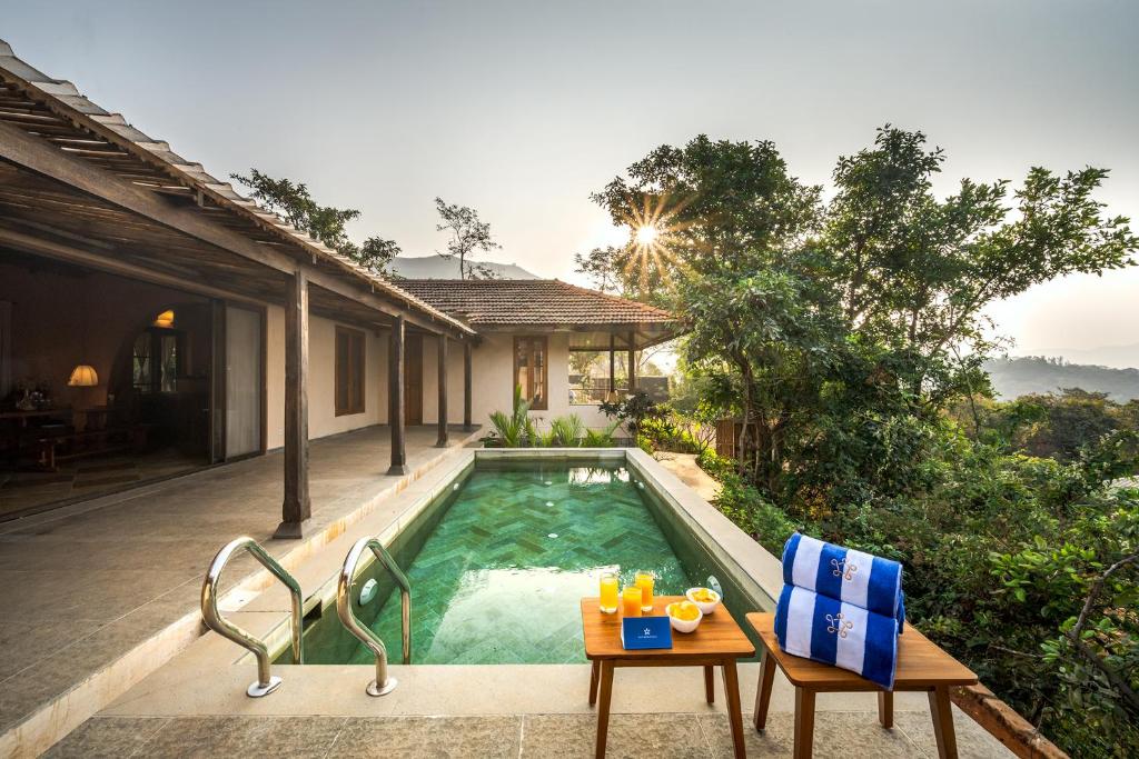 a pool with two chairs and a table next to a house at SaffronStays Rustic Trails in Mulshi