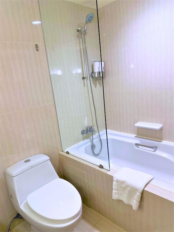 A compact tiled bathroom with a toilet and a bathtub fitted with a handheld shower.