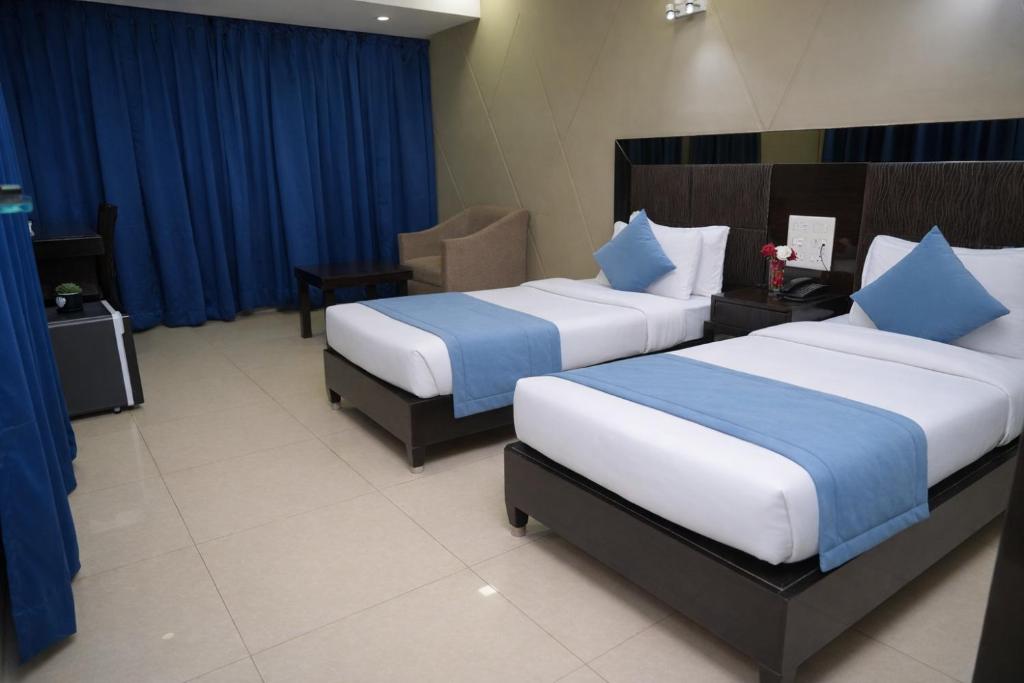 two beds in a hotel room with blue curtains at Hema's Hotel Supreme in Visakhapatnam