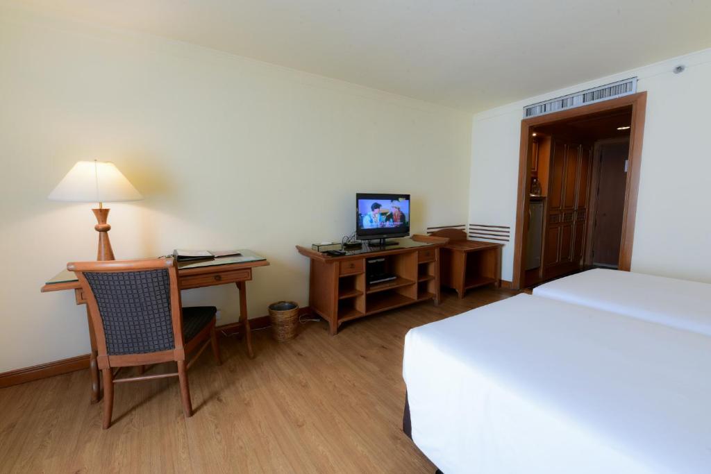 A bedroom view showing a narrow wooden desk, chair, television and storage furniture.