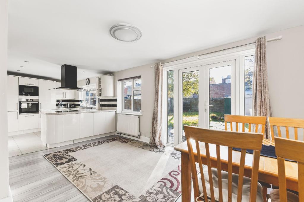 a kitchen with white cabinets and a dining room with a table at Spacious 4BDR House with Parking by Heathrow in Hillingdon