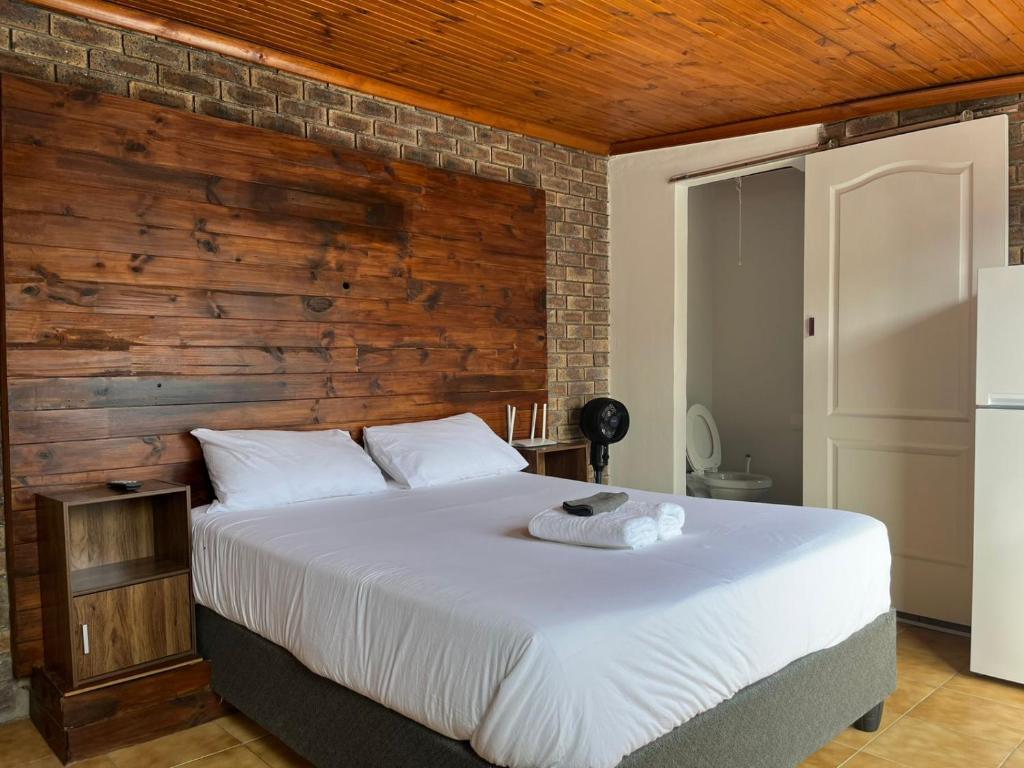 a bedroom with a white bed with a wooden wall at Blue Moon Cozy Poolside Bachelor Flat in Bellville