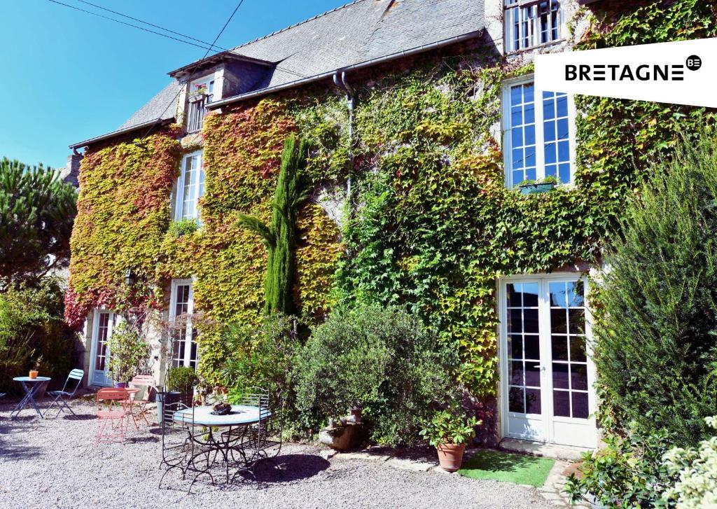 a building covered in ivy with a table and chairs at LA VALLÉE DU LAUNAY GiTES in Taden