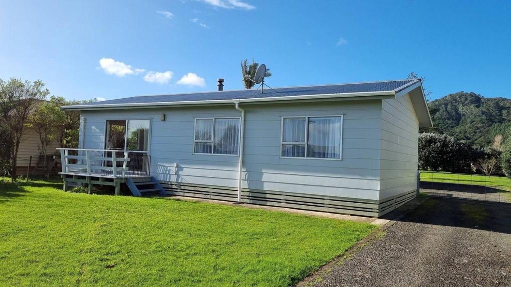 a small white house with a grass yard at Hooked On Tiki in Coromandel Town