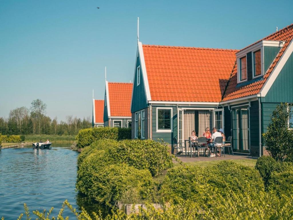 a house with people sitting at a table next to the water at Charming Chalet in De Rijp in West-Graftdijk