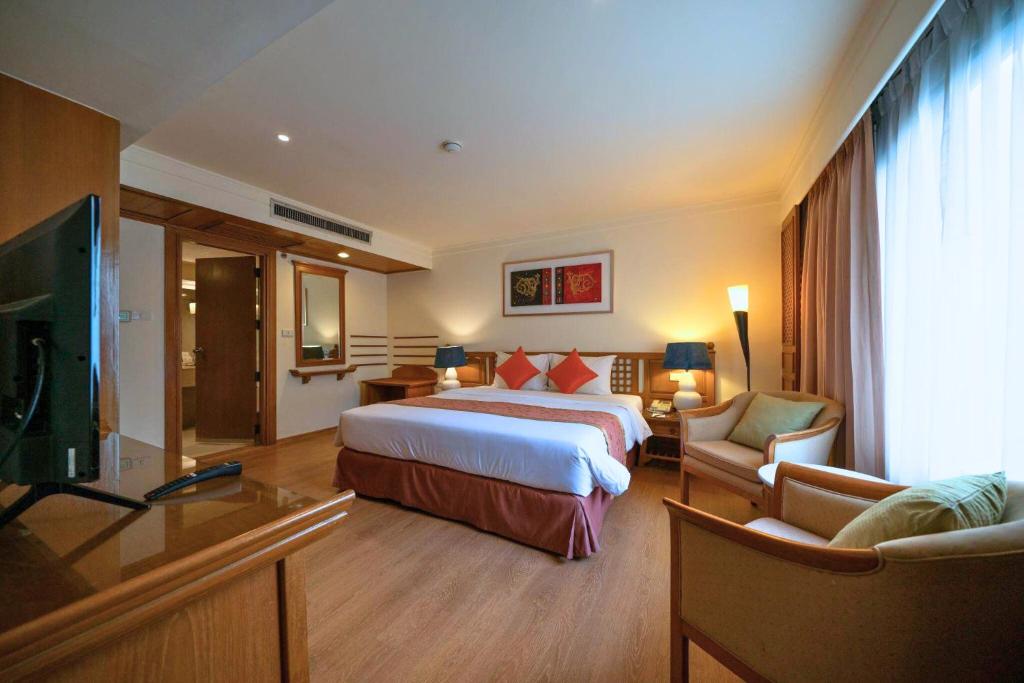 A spacious bedroom with a large bed, television, two armchairs, and a full-height curtained window.
