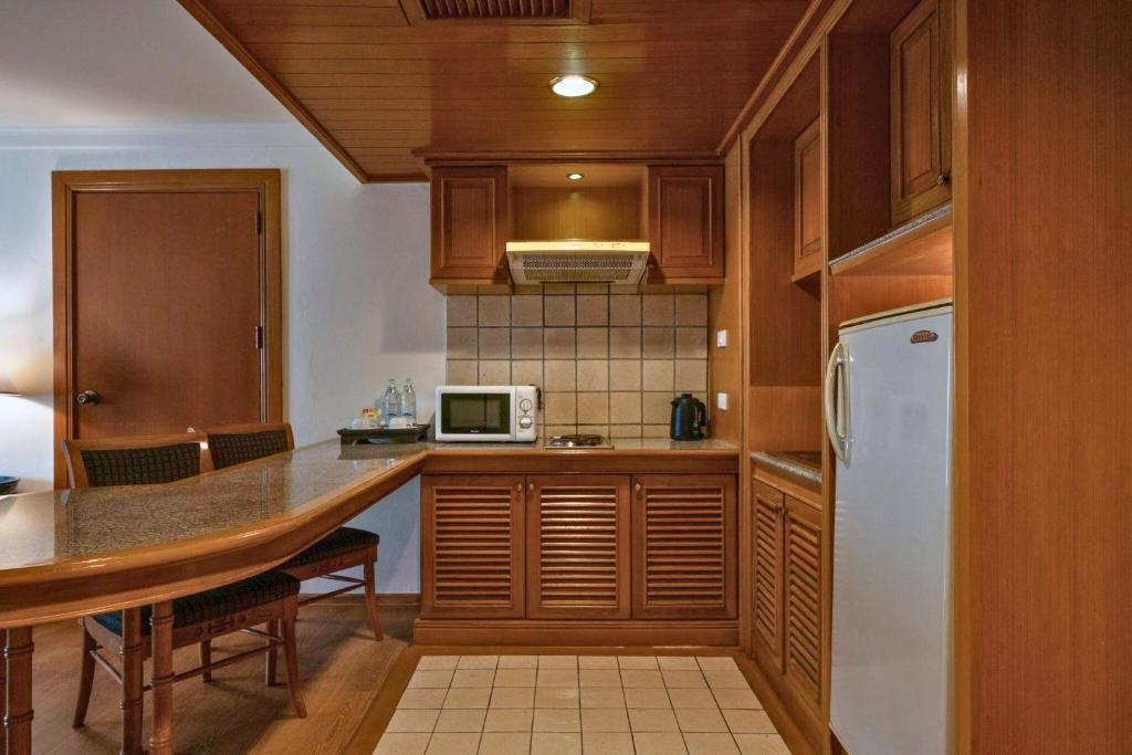 A compact wood-finished kitchenette with a refrigerator, microwave, kettle, and two-seat table.