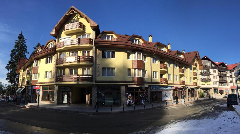 a large yellow building on a street with snow on the ground at GM Royal Plaza in Borovets