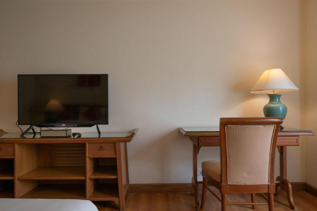 A wooden writing desk and television share a wall opposite the bed.