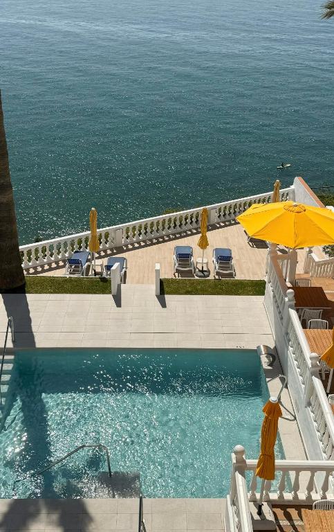 a swimming pool with an umbrella and the ocean at Hotel Paraíso Del Mar in Nerja