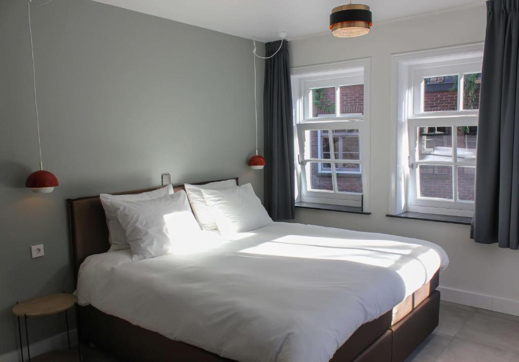 een slaapkamer met een bed met witte lakens en 2 ramen bij Boutique Hotel Nieuw Uilenburg in Den Bosch
