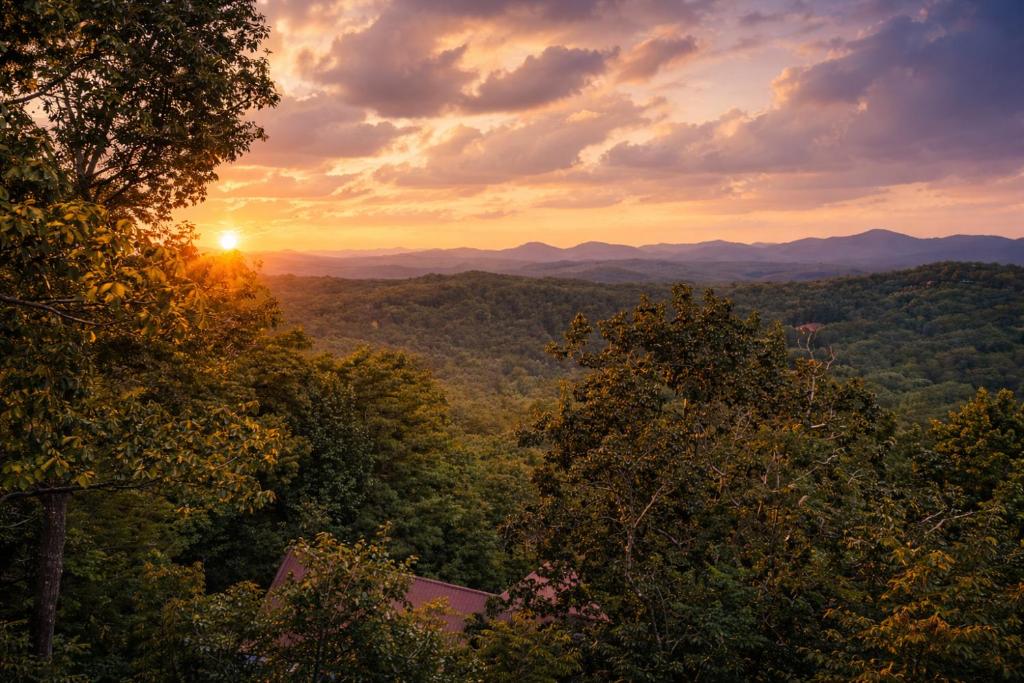 a sunset in the mountains with trees in the foreground at Bella Vista! Long range MTN views, Hot Tub, Close to town and Lake in Blue Ridge