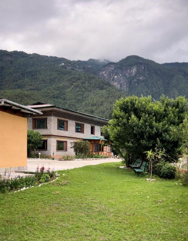 a building with a tree and mountains in the background at Taktshang Paradise in Paro