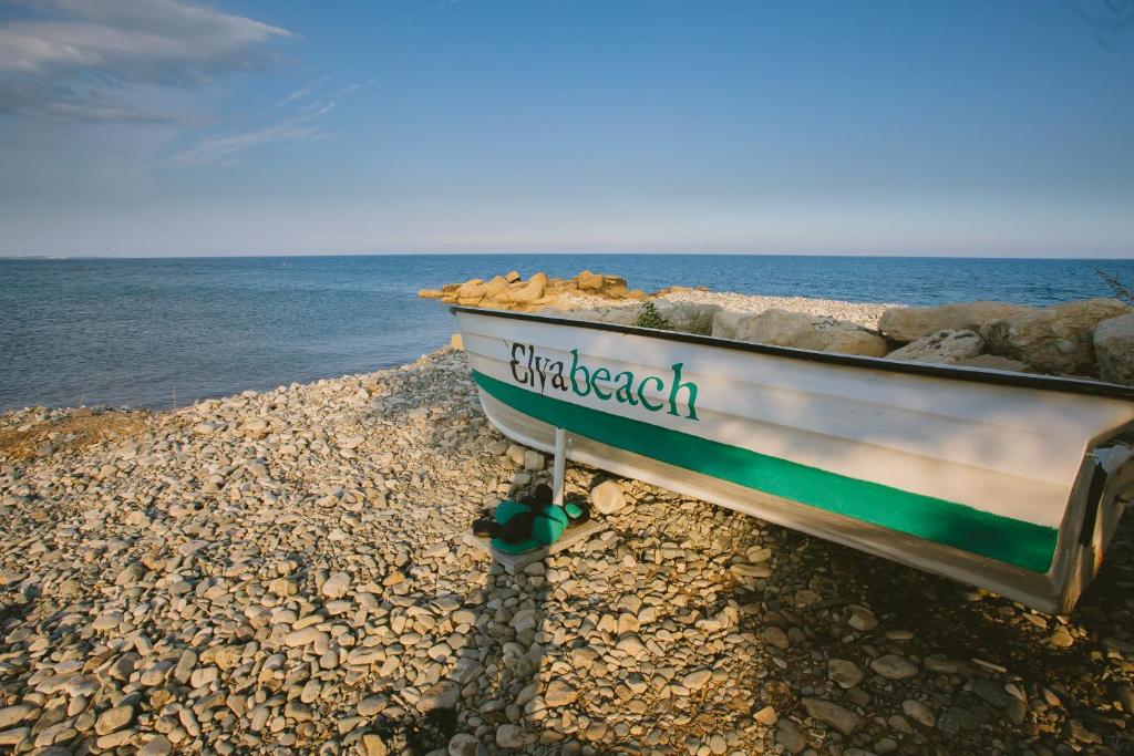a boat sitting on a rocky beach next to the ocean at Elya Beach Luxury Suites in Ayios Theodhoros