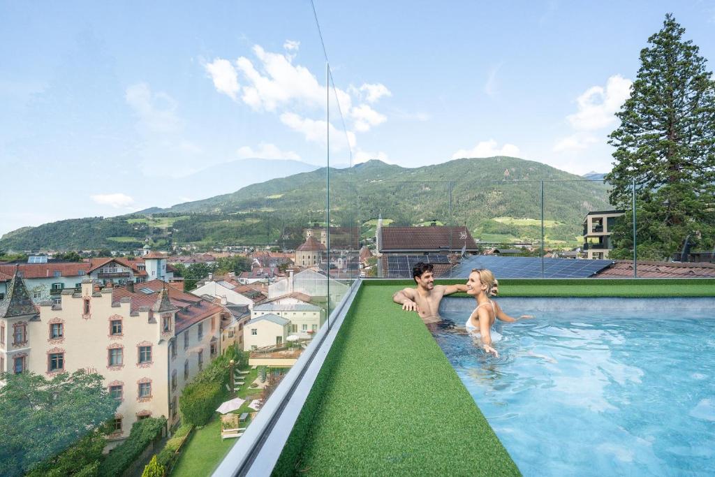 a couple sitting on the edge of a swimming pool at Dominik Alpine City Wellness Hotel Brixen - Adults only in Bressanone