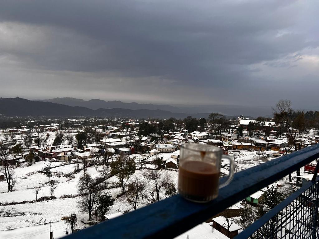 a cup of coffee sitting on a balcony with a snow covered city at Hill Veu Home Bir Billing in Bīr