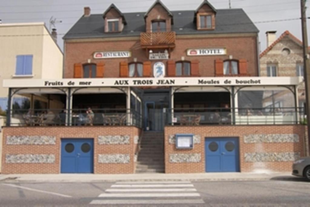 een bakstenen gebouw met blauwe deuren in een straat bij Aux Trois Jean in Le Crotoy