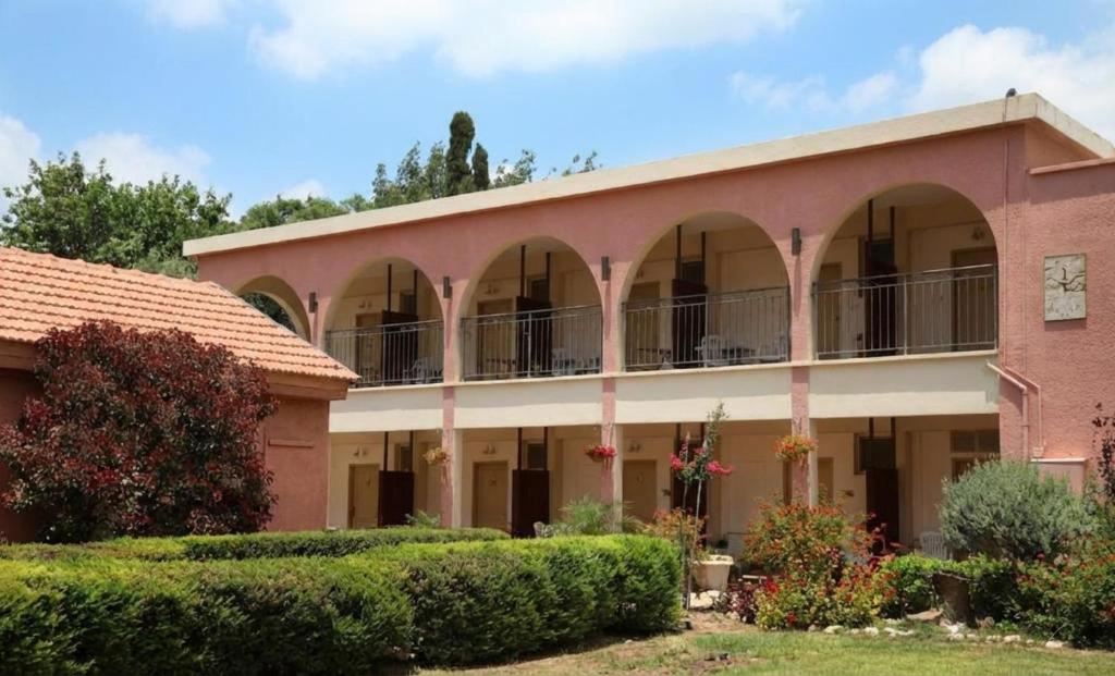 a building with arches and bushes in front of it at El Mul Golan Kibbutz Country Lodging in Shaar Hagolan