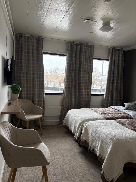 a bedroom with two beds and a desk and two windows at Hotel Sommarvind in Inkoo