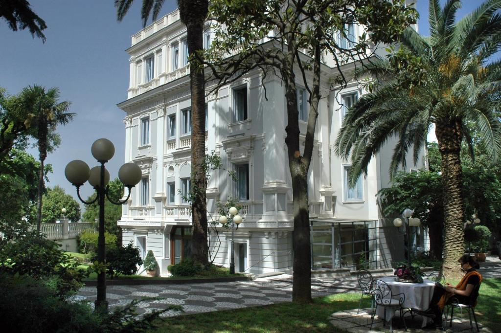 uma mulher sentada numa mesa em frente a um edifício branco em Hotel Flora em Frascati