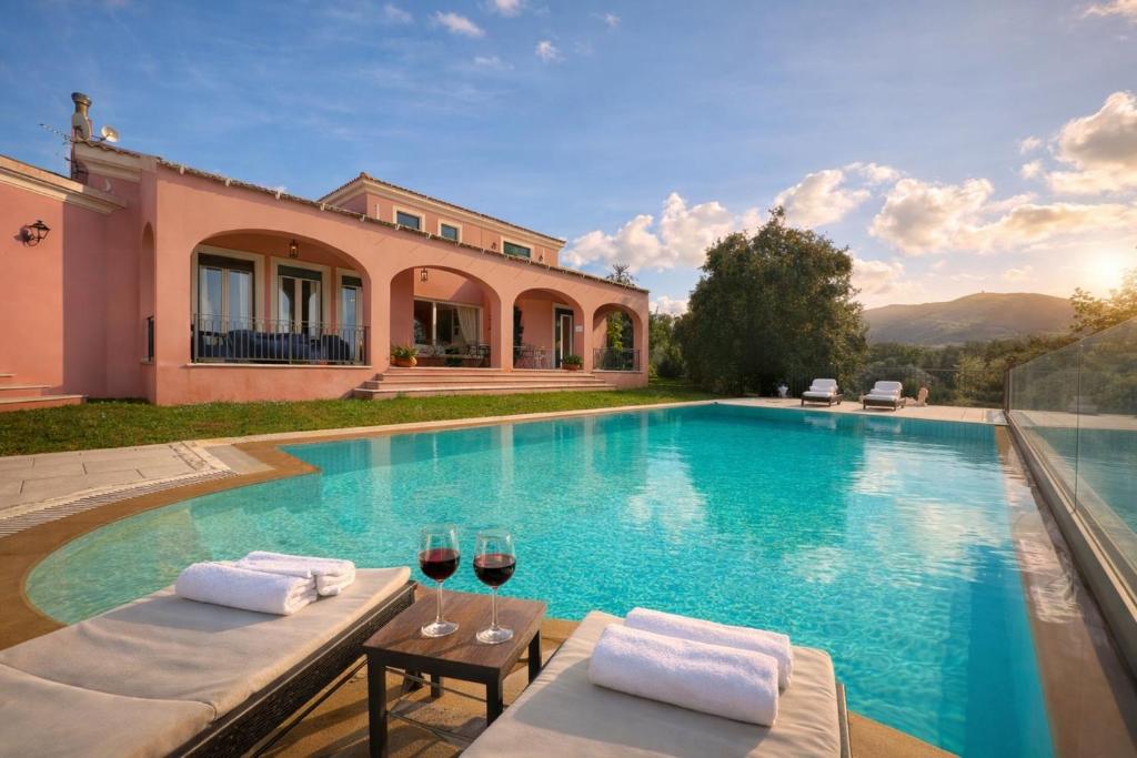 a house with a swimming pool with two glasses of wine at Villa Olea Corfu - Private Pool & Panoramic Views in Perama
