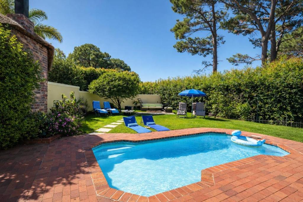 a swimming pool in a yard with blue chairs and an umbrella at 3 Bedroom Family Home, Pool & Garden, Upper Constantia in Constantia