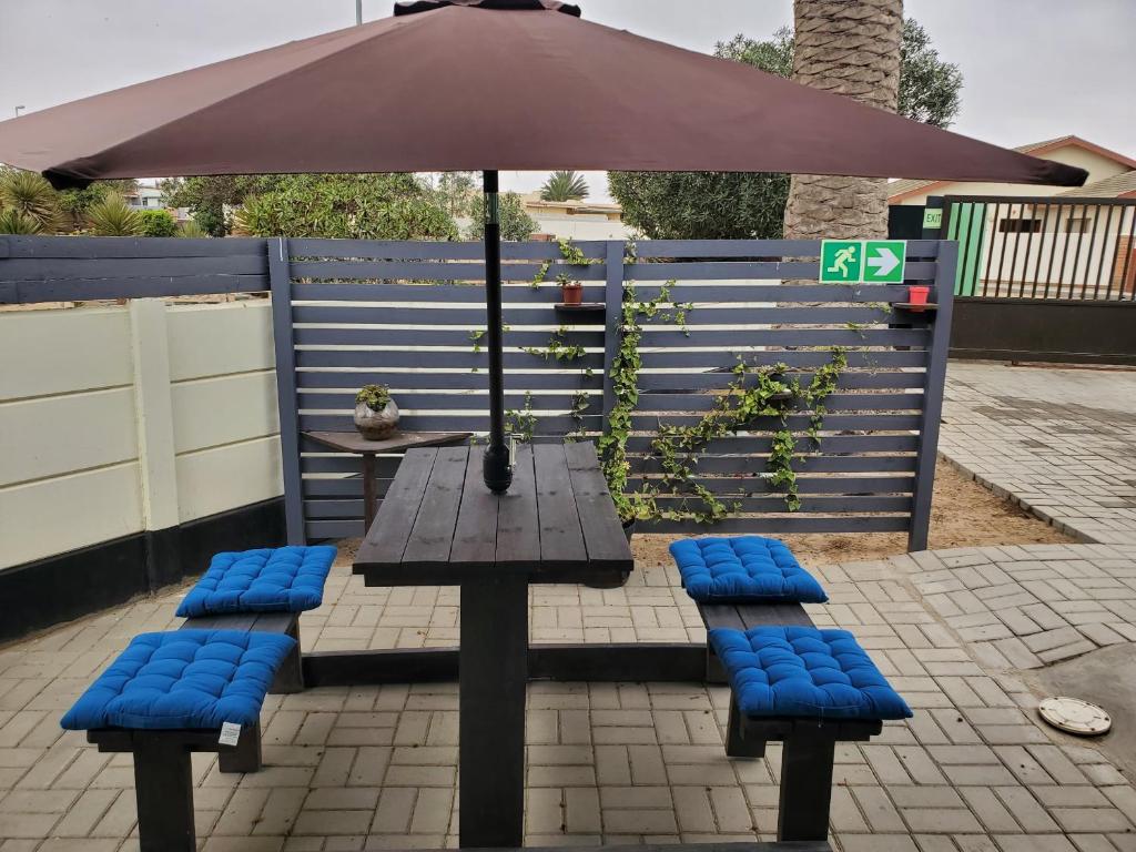 a picnic table with blue cushioned chairs and an umbrella at Casa de Marcos in Swakopmund