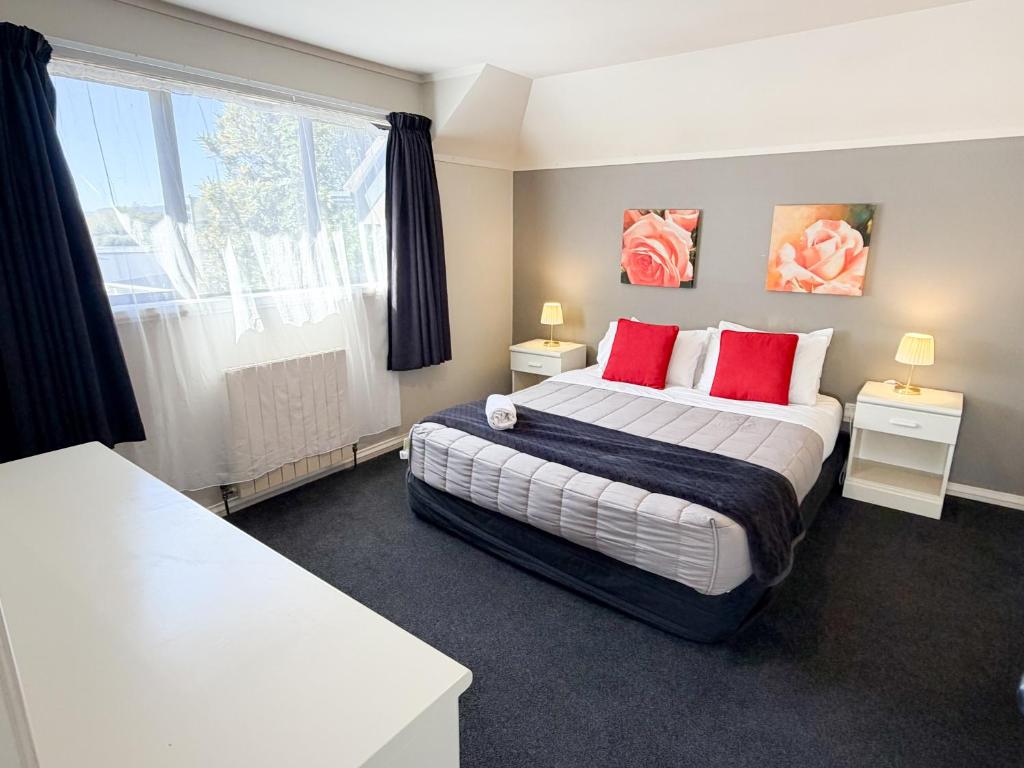 a bedroom with a bed with red pillows and a window at Champers Motor Inn in Lower Hutt