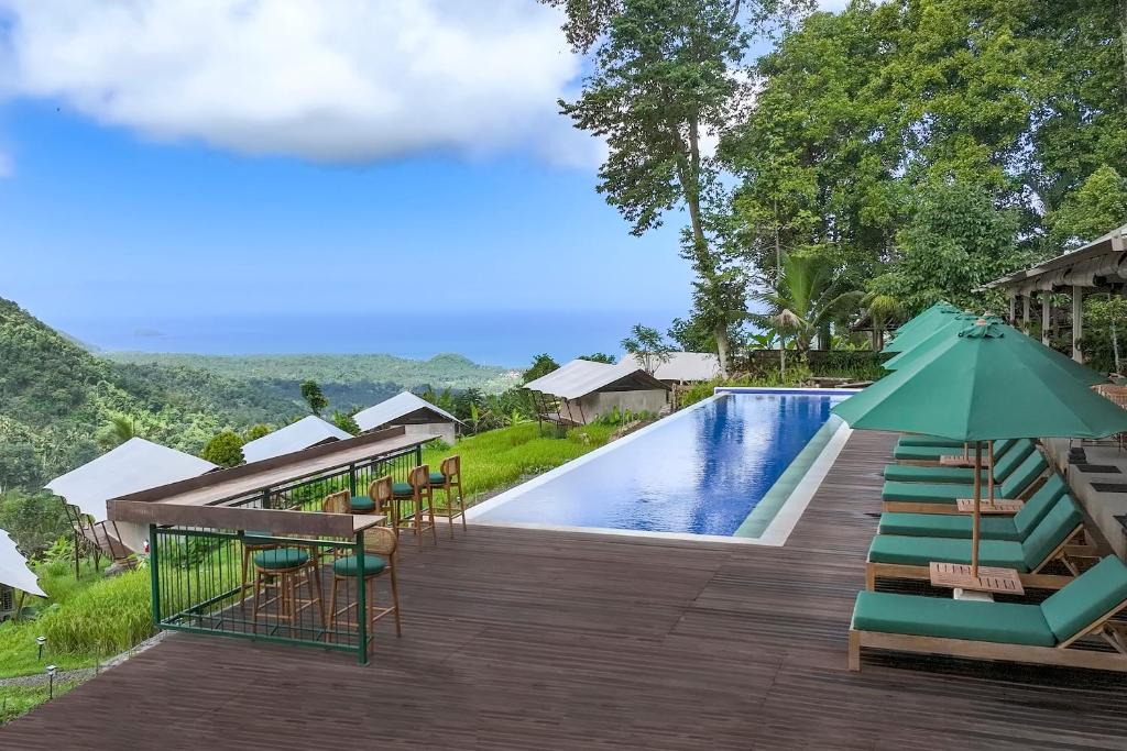 a pool at the resort with chairs and an umbrella at Kaura Manggis, Bali - Luxury Tent in Candidasa