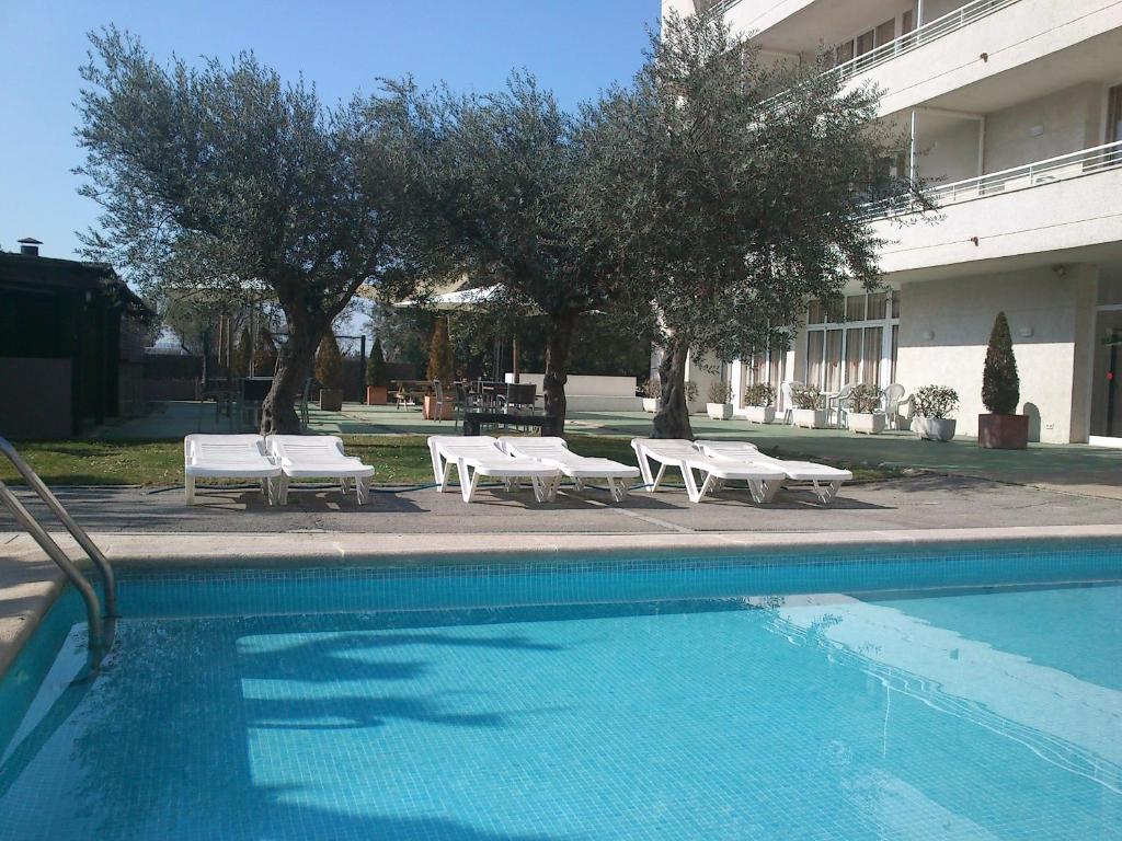 uma piscina com bancos brancos e árvores ao lado de um edifício em Apartamentos Miami em L'Estartit