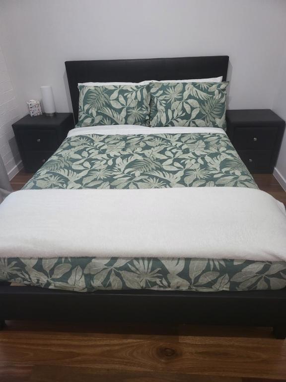 a bed with a green and white comforter and pillows at Treasure in Karabah in Queanbeyan