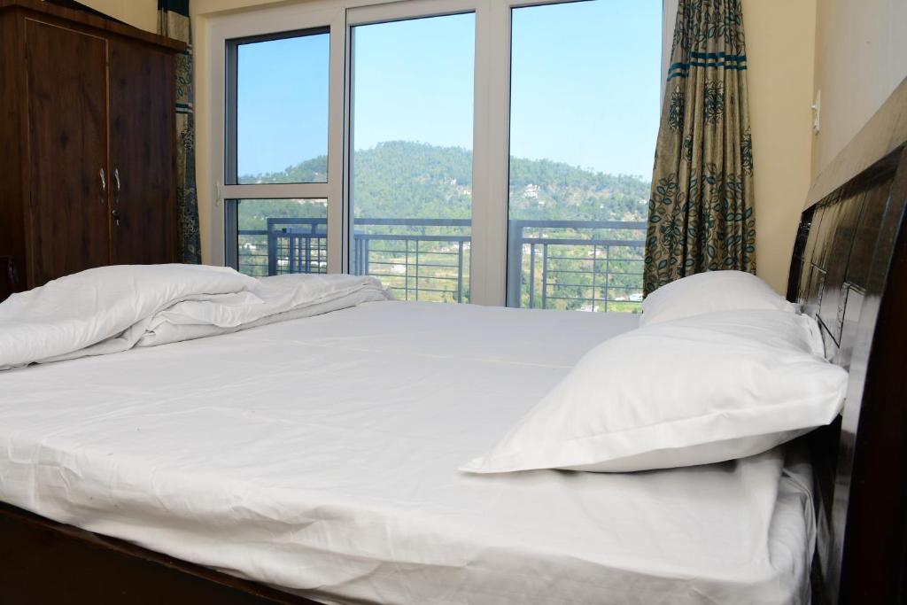 a bed with white sheets and pillows in front of a window at Serenidad- The Cottage in Mukteshwar
