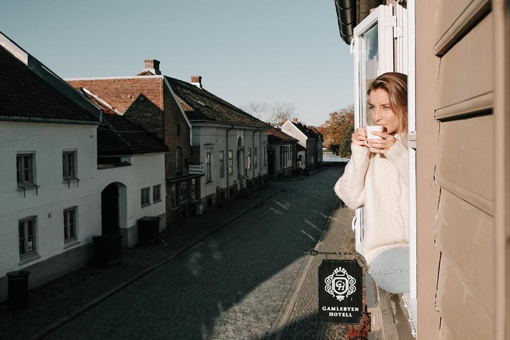 a woman is looking out of a window while holding a cup at Gamlebyen Hotell - Fredrikstad in Fredrikstad