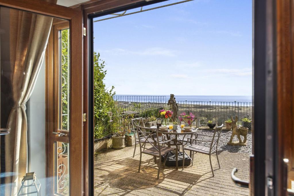 a patio with a table and chairs and a view of the ocean at Bay View - holiday cottage by the sea with stunning views in Pendine