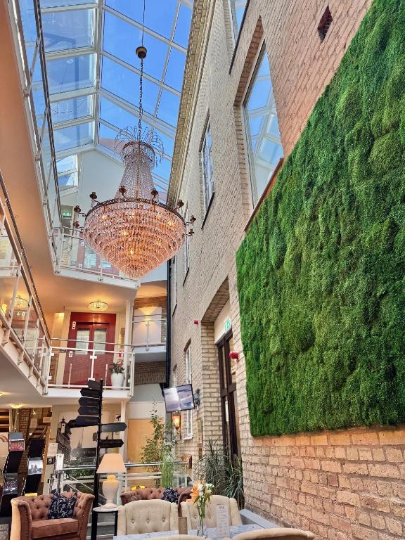 Przestronne atrium hotelowe z kryształowym żyrandolem, zieloną ścianą roślinną i kącikiem wypoczynkowym.